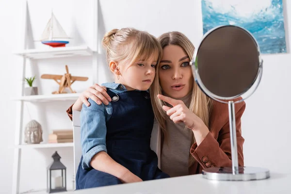 Speech therapist pointing with finger near pupil and mirror in classroom — Stock Photo