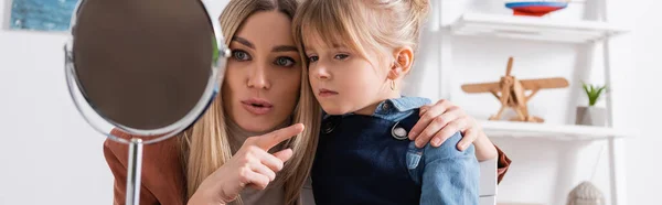 Terapeuta del habla señalando con el dedo cerca del niño y el espejo en el aula, pancarta - foto de stock