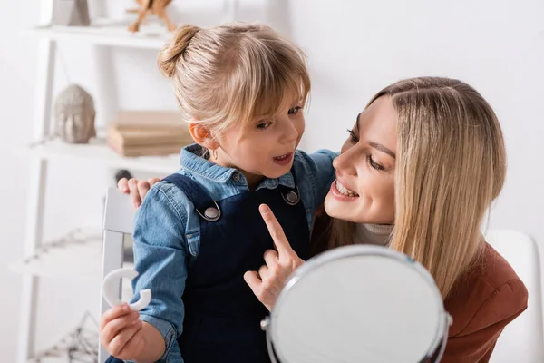 Terapeuta del habla positiva apuntando a la pupila con letra cerca del espejo en el aula - foto de stock