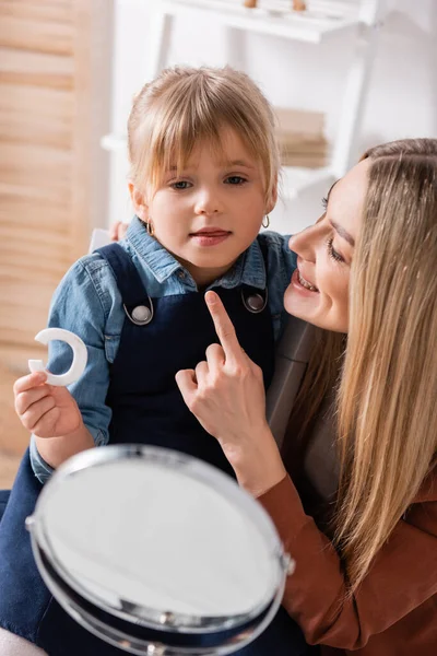 Speech therapist che punta con il dito al bambino con lettera vicino allo specchio in classe — Foto stock