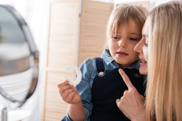 Alumno sosteniendo carta mientras habla cerca logopedista y espejo en el aula — Stock Photo