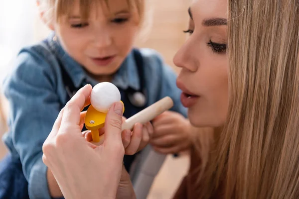 Speech therapist holding respiratory muscle trainer near blurred girl in classroom — Stock Photo