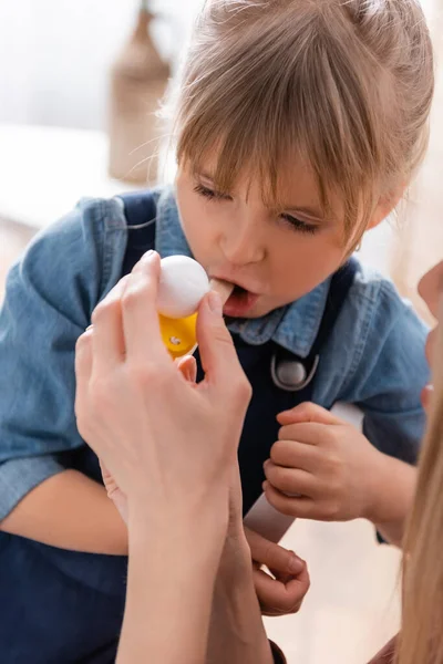 Terapeuta del habla sosteniendo entrenador muscular respiratorio cerca del niño durante la lección en el aula - foto de stock