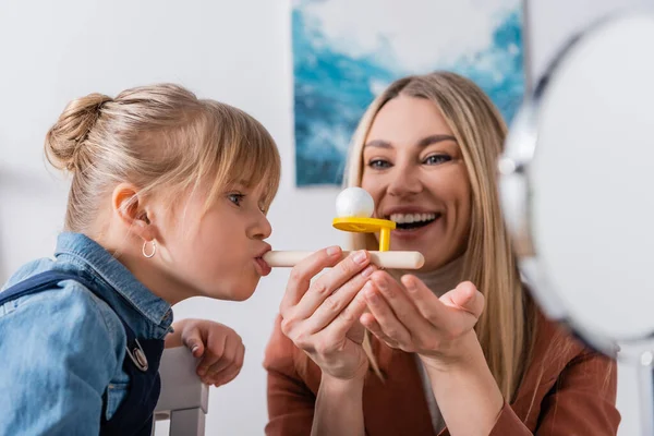 Pupil training with respiratory muscle trainer near cheerful speech therapist in classroom — Stock Photo