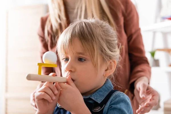 Enfant utilisant un entraîneur de muscles respiratoires pendant la leçon près du logopédiste en classe — Photo de stock