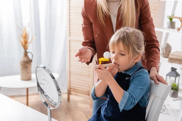 Chica usando entrenador de músculos respiratorios cerca de espejo y terapeuta del habla en el aula — Stock Photo