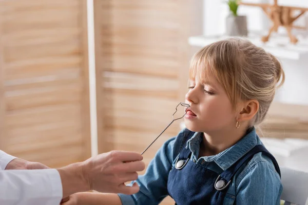 Speech therapist in white coat holding tool near kid in classroom — Stock Photo