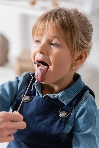 Orthophoniste tenant une sonde logopédique près d'un enfant qui sort la langue en classe — Photo de stock