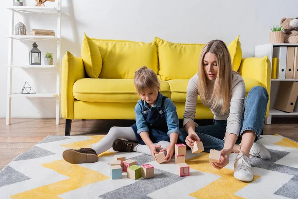 Logopedista sosteniendo bloques de madera con letras cerca del niño en la sala de consulta - foto de stock