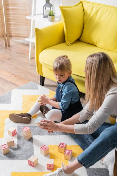 Girl sitting near speech therapist with wooden blocks on carpet in consulting room — Stock Photo