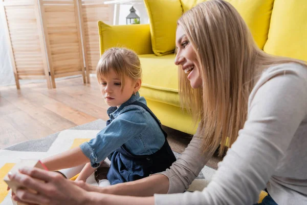 Sonriente terapeuta del habla sosteniendo un bloque de madera cerca de un niño en la sala de consulta - foto de stock