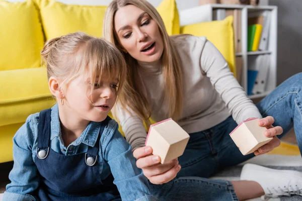 Speech therapist holding wooden blocks during lesson with girl in consulting room — Stock Photo