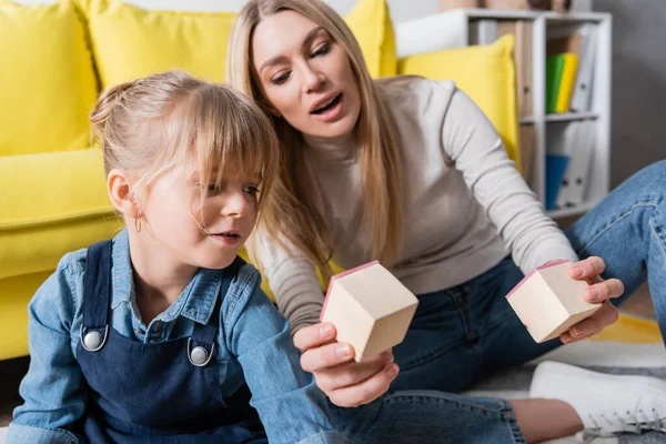 Orthophoniste tenant des blocs de bois pendant le cours avec la fille dans la salle de consultation — Photo de stock