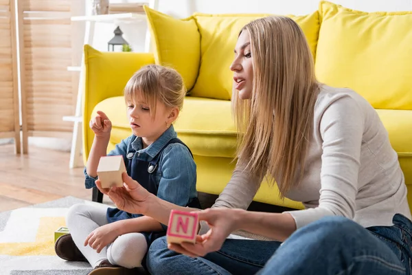 Bambino che punta con dito vicino logopedista con blocchi di legno in sala di consultazione — Foto stock