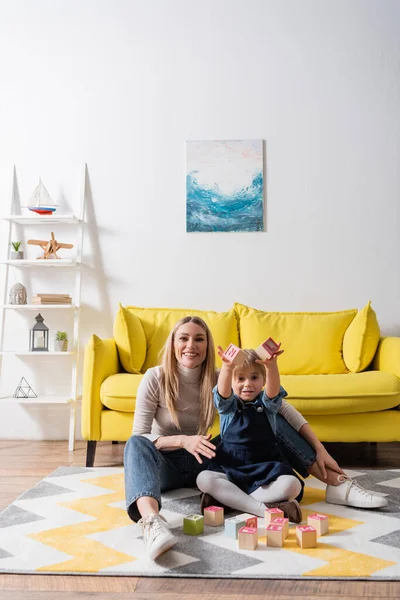 Positives Kind hält Holzklötze mit Buchstaben in der Nähe des Logopäden im Sprechzimmer — Stockfoto