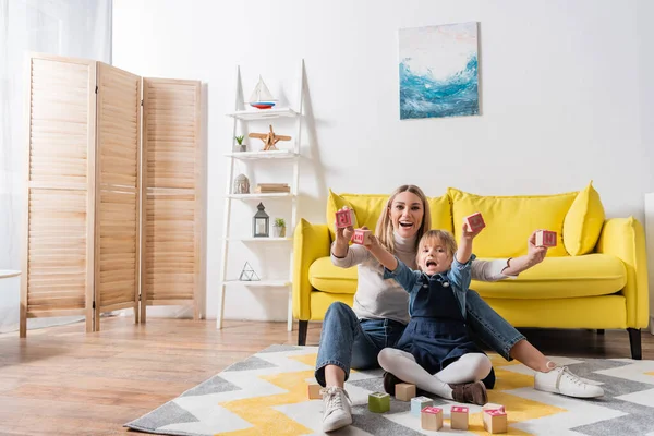 Alegre terapeuta del habla sosteniendo bloques de madera con letras cerca de la chica en la sala de consulta — Stock Photo
