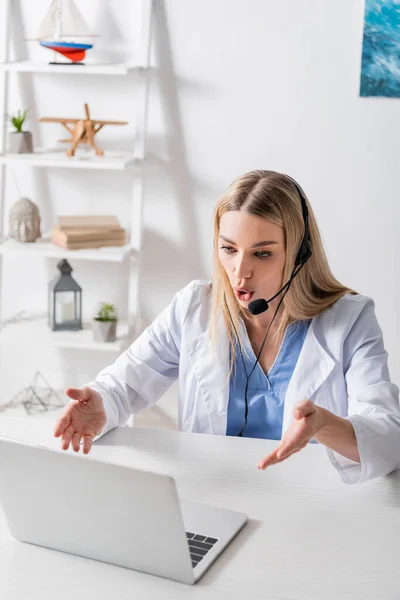 Speech therapist in headset having video call on laptop in consulting room — Stock Photo