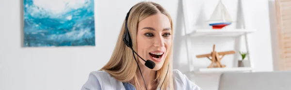 Logopedista positivo en auriculares con videollamada en portátil en sala de consulta, pancarta - foto de stock