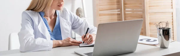 Обрезанный взгляд логопеда, пишущего на ноутбуке рядом с ноутбуком и буфером обмена в консультационной комнате, баннер — стоковое фото