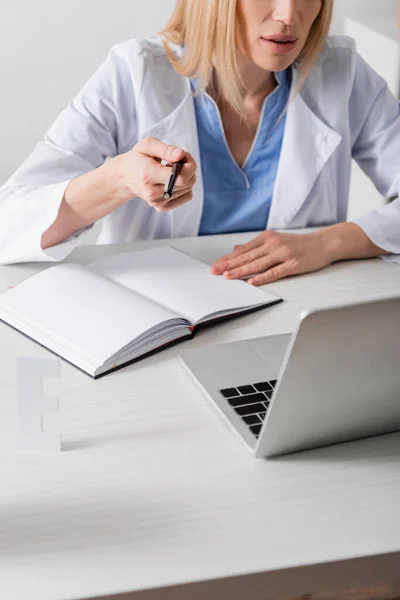 Vista recortada do fonoaudiólogo segurando caneta perto de notebook e laptop em consultório — Fotografia de Stock