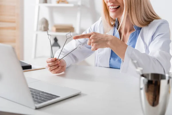 Cropped view of smiling speech therapist pointing at tools during video call on laptop in consulting room — Stock Photo