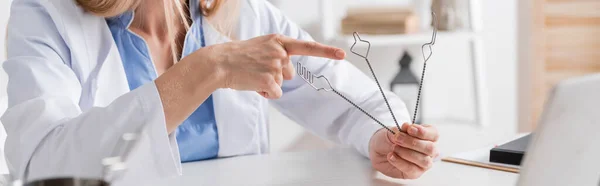 Vista recortada del logopedista apuntando a las herramientas cerca de la computadora portátil borrosa en la sala de consulta, pancarta - foto de stock