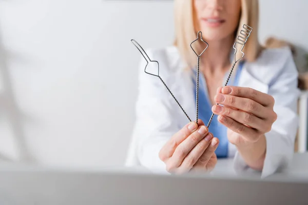 Ausgeschnittene Ansicht der Werkzeuge in den Händen eines verschwommenen Logopäden, der in der Nähe des Laptops im Sprechzimmer arbeitet — Stockfoto