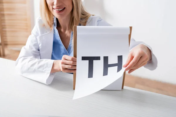 Vista recortada do fonoaudiólogo sorridente segurando prancheta com letras no consultório — Fotografia de Stock