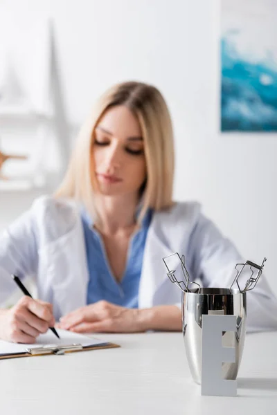 Herramientas y cartas cerca de la escritura logopedista borrosa en el portapapeles en la sala de consulta - foto de stock