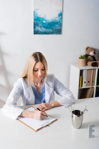 Logopädin schreibt auf Klemmbrett in der Nähe von Metallwerkzeugen im Sprechzimmer — Stockfoto