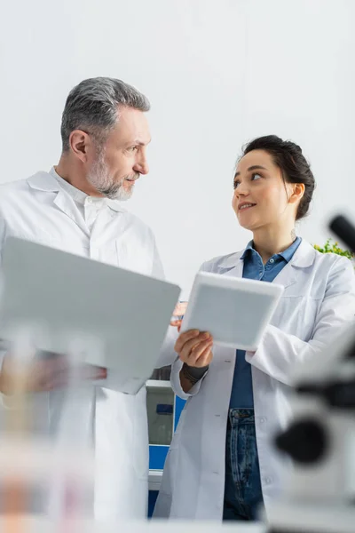 Cientistas em casacos brancos segurando gadgets e falando em laboratório — Fotografia de Stock