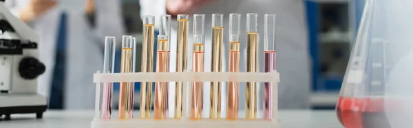 Selective focus of test tubes with liquid near cropped bioengineers on blurred background, banner — Stock Photo
