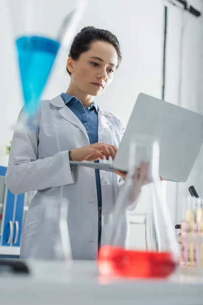 Vista de ángulo bajo del bioingeniero en la capa blanca que sostiene el ordenador portátil en el primer plano borroso - foto de stock