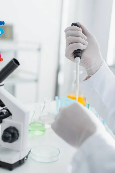 Cropped view of bioengineer with micropipette working near blurred microscope — Stock Photo