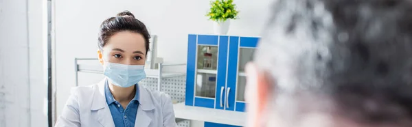 Young geneticist in medical mask looking at colleague on blurred foreground, banner — Stock Photo