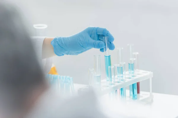 Partial view of geneticist holding test tube with blue liquid on blurred foreground — Stock Photo