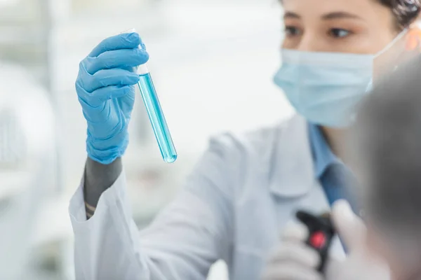 Bioengenheiro desfocado em máscara médica segurando tubo de ensaio em laboratório — Fotografia de Stock