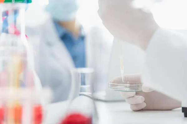 Cropped view of scientist with pipette and petri dish on blurred background — Stock Photo