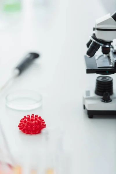 Red coronavirus bacteria model and blurred microscope in bio laboratory — Stock Photo