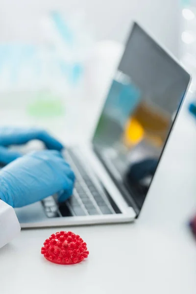 Partial view of virologist typing on laptop with blank screen near red coronavirus bacterial model — Stock Photo