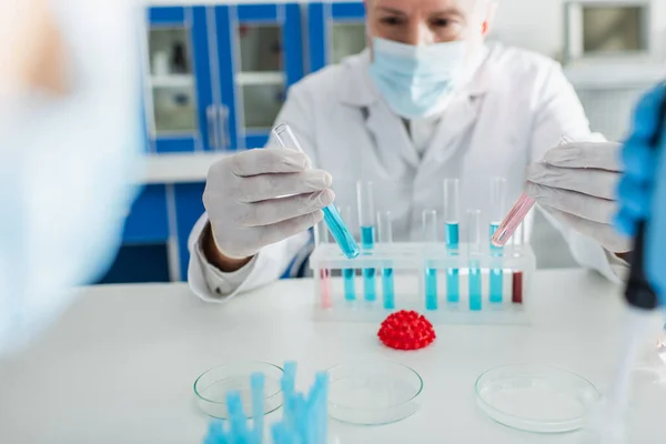 Bioingeniero sosteniendo tubos de ensayo con líquido cerca del modelo de bacterias coronavirus - foto de stock