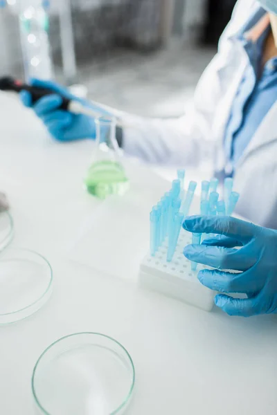 Vista recortada del genetista borroso en guantes de látex cerca de tubos de ensayo - foto de stock