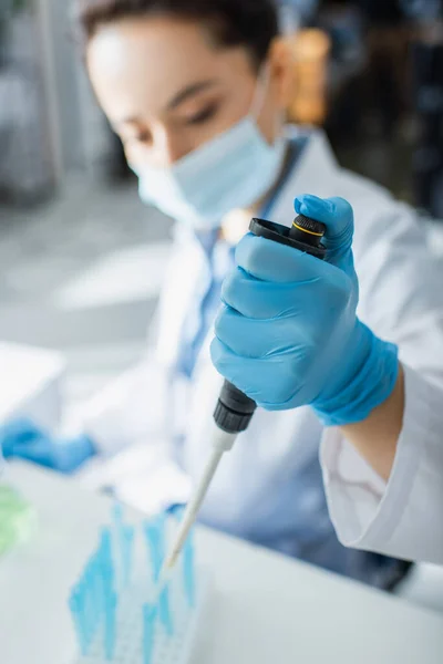 Blurred geneticist in medical mask working with micropipette in lab — Stock Photo