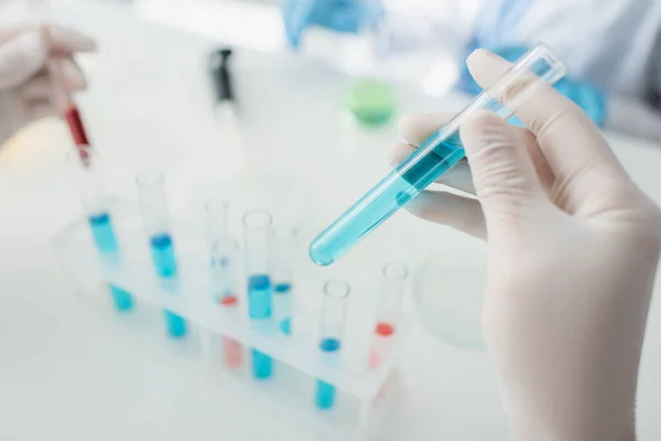 Cropped view of scientist holding test tube with blue liquid on blurred background — Stock Photo