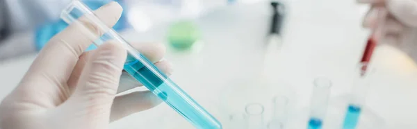 Vista parcial del científico en guante de látex sosteniendo tubo de ensayo con líquido azul, bandera - foto de stock