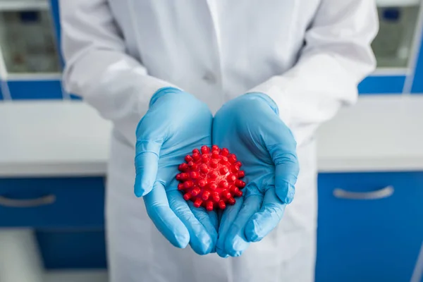Vista ritagliata del biologo in guanti di lattice blu con modello di batteri coronavirus rosso — Foto stock