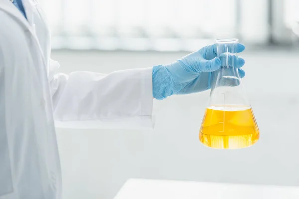 Cropped view of woman in latex glove holding flask with yellow liquid — Stock Photo