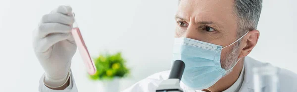 Scienziato maturo in maschera medica che tiene la provetta con liquido, banner — Foto stock