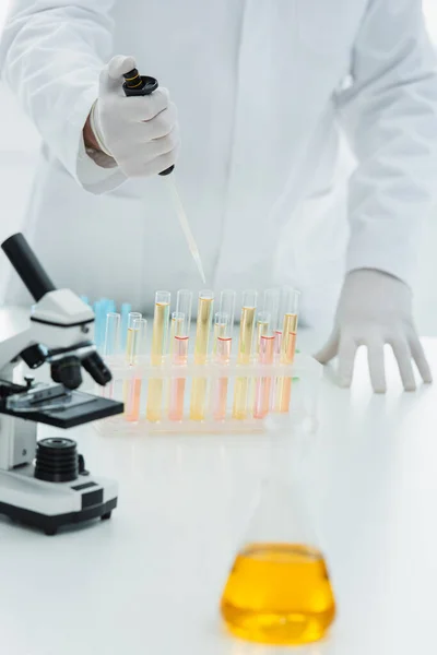 Cropped view of geneticist using micropipette near test tubes and microscope — Stock Photo