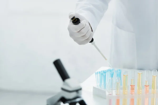 Visão recortada de bioengenheiro segurando micropipeta perto de tubos de ensaio com líquido — Fotografia de Stock